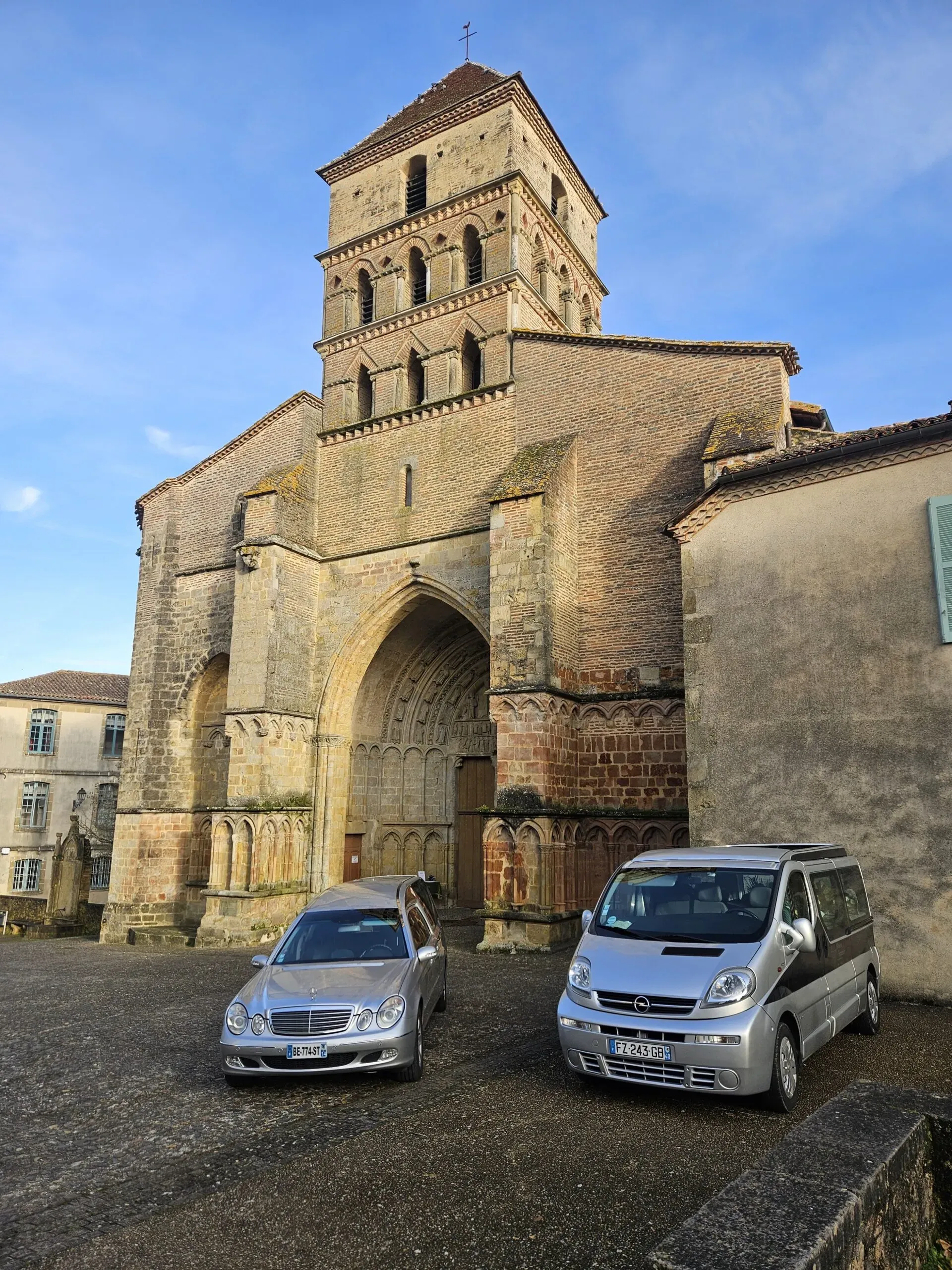 Véhicules funéraires stationnés devant le parvis d'une église historique en pierre.