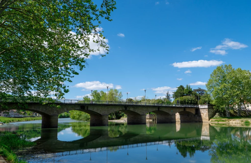 Pont en pierre au-dessus d'une rivière calme sous un ciel bleu ensoleillé.